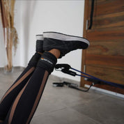 A person's leg is seen with the A90 Leg Day Set around the ankle, performing leg exercises indoors. The focus is on the stretch and flexing of the muscles during the workout.